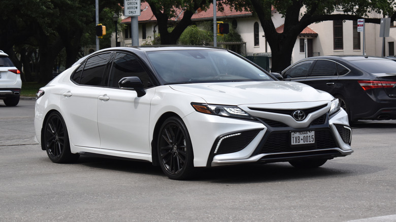 A white Toyota Camry sedan traveling down a highway in moderate traffic.