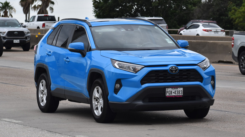 A blue Toyota RAV4 traveling down a highway in moderate traffic.