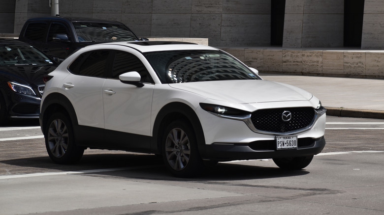 A portrait of a white Mazda CX SUV traveling in a downtown district