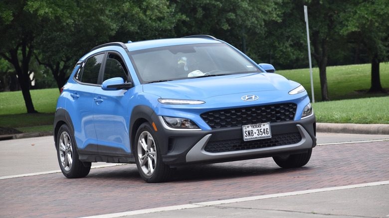 A blue Honda Kona crossover SUV cruising near a nature reserve.