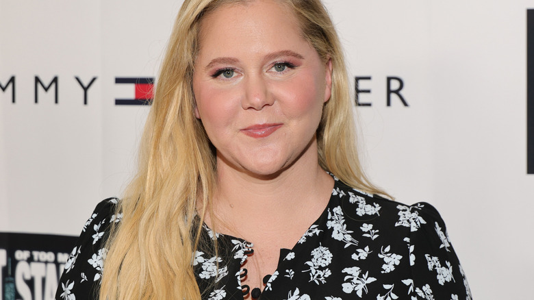 Amy Schumer smiling in front of white Tommy Hilfiger back drop
