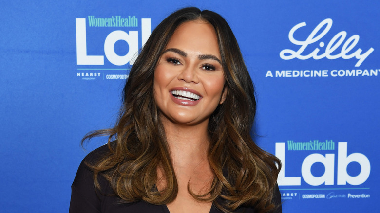 Model Chrissy Teigen smiles as she poses in front of blue back drop