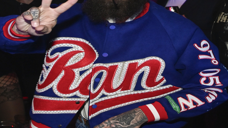 Post Malone wearing white had and smiling while making peace sign