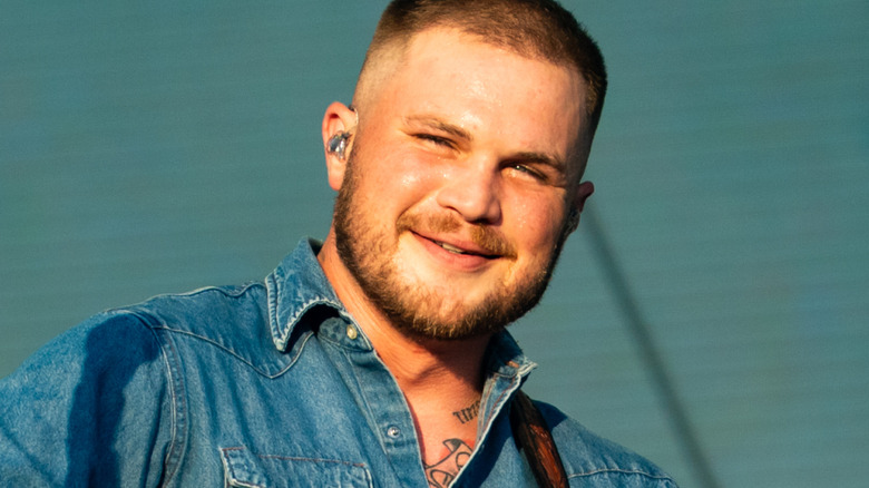 Zach Bryan smiles as he performs on stage