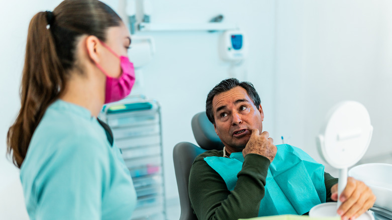 Senior man sitting in a detist's chair discussing a problem with a tooth with a hygienist