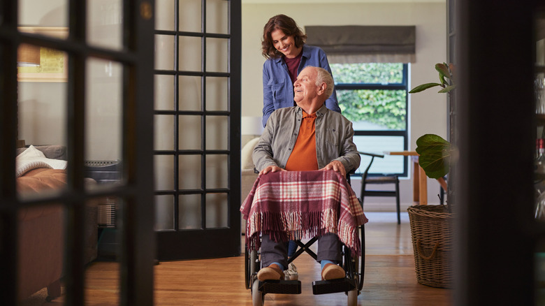 Senior man sitting on a wheelchair while his daughter assists him.