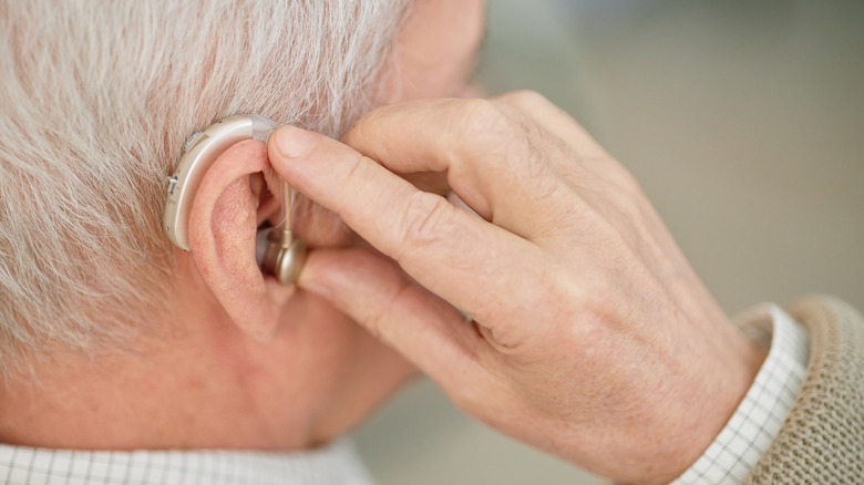 Close-up image of elderly person adjusting hearing aid behind ear.