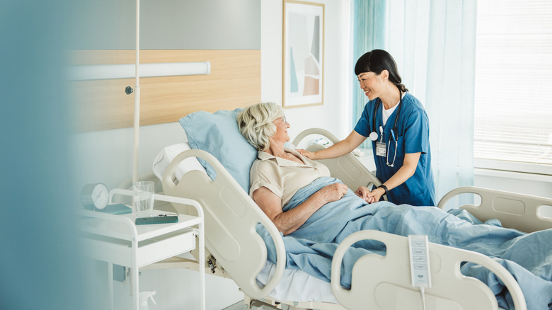Nurse talking to senior woman in hospital bed.