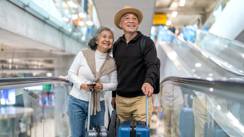 Senior couple smiling in an airport with suitcases and excited looks on their faces