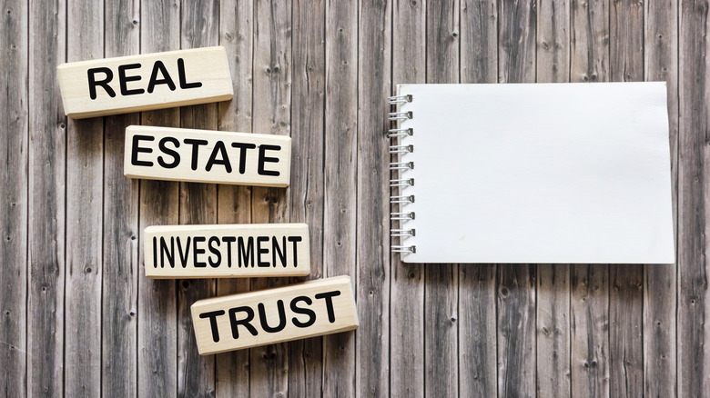 Conceptual words REIT real estate investment fund on wooden blocks on a wooden background next to a notepad for text.