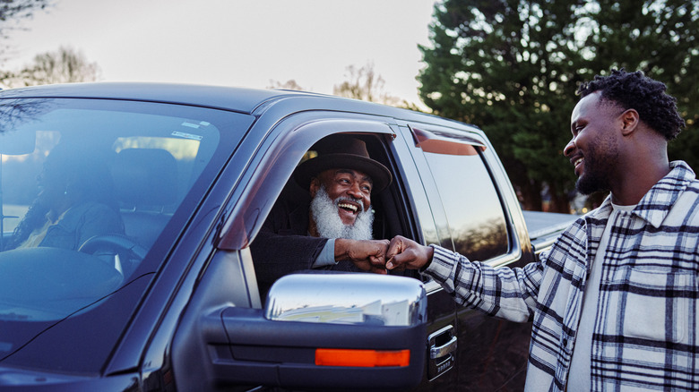 A joyful and active senior Black man sits in the driver's seat of a pickup truck