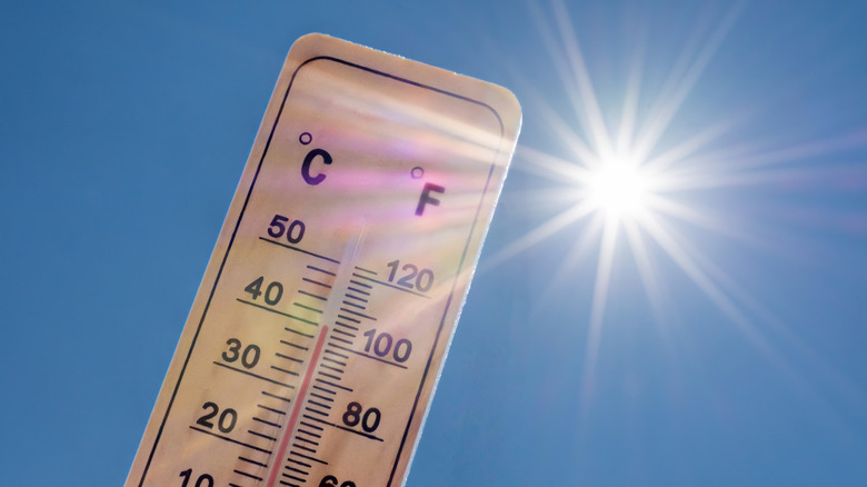 Thermometer displaying a high temperature in degrees Celsius and Fahrenheit with a radiant sun on a background of blue sky.
