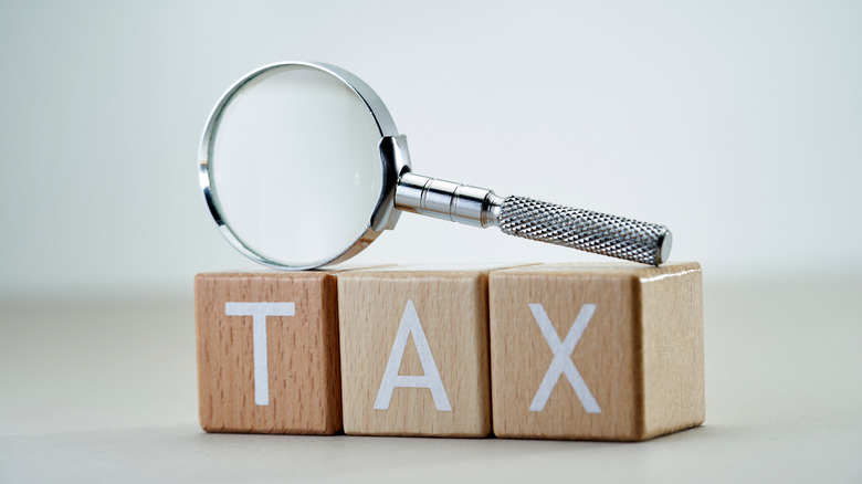 Three wooden blocks spelling the word tax with a magnifying glass resting on top