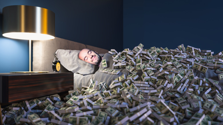 A man laying in bed while covered a huge pile of cash