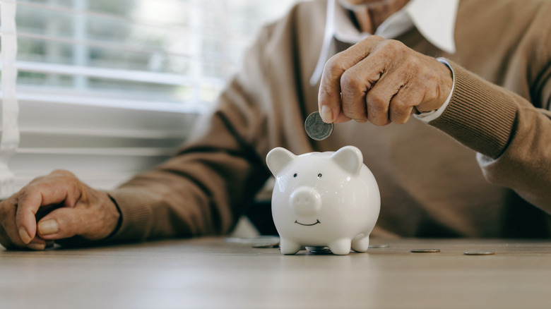 An old man hand putting money coins in a piggy bank.