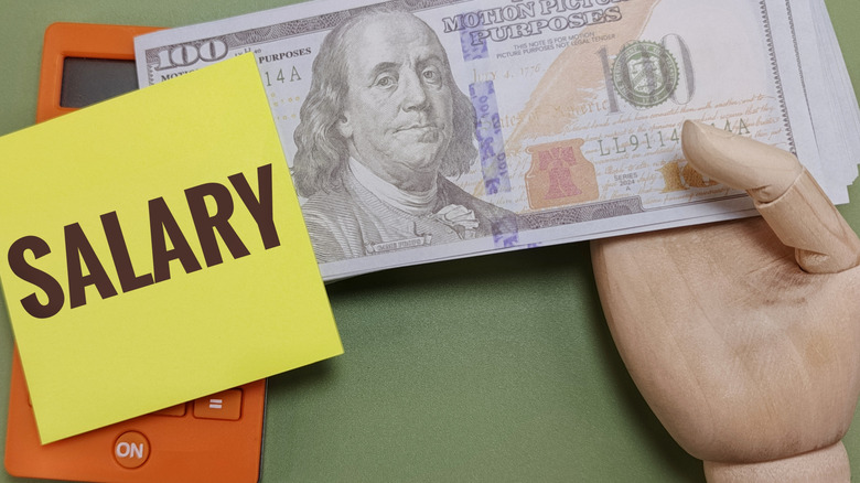 salary written on sticky note next to $100 bills