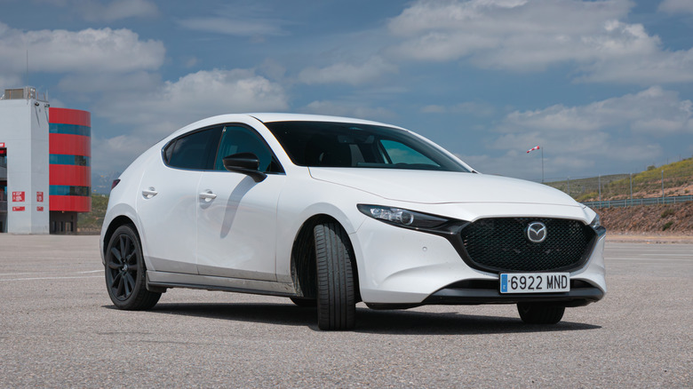 A white Mazda 3 in an empty parking lot.