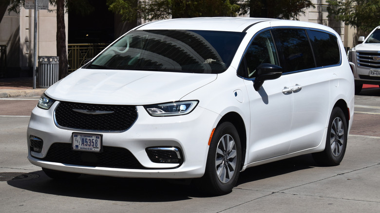A white Chrysler Pacifica minivan in the downtown financial district near a residential skyscraper.