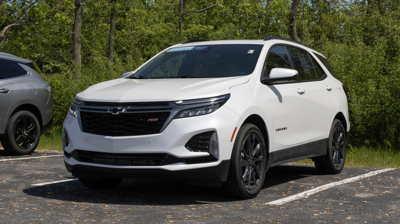 A used white Chevrolet Equinox on display in front of a wooded area.