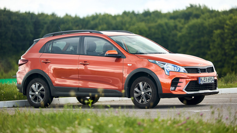 An orange Kia Rio reverse parked in a heavily wooded area