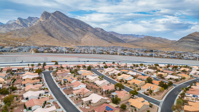 Aerial view of a suburban neighborhood in Las Vegas with a backdrop of mountains under a cloudy sky.