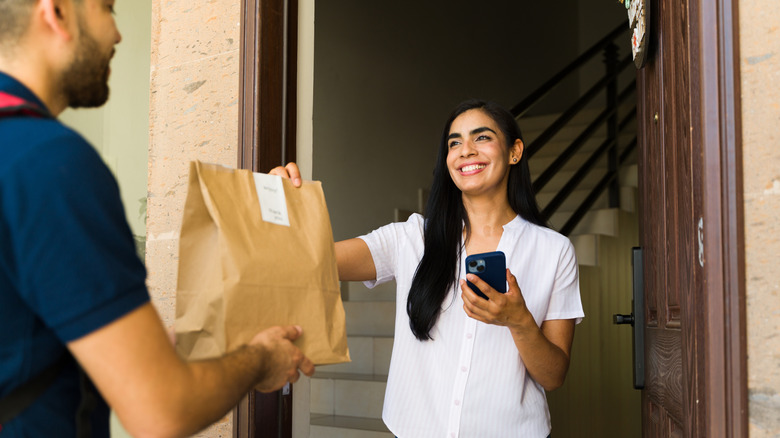 A food delivery person handing bagged food over to a customer.
