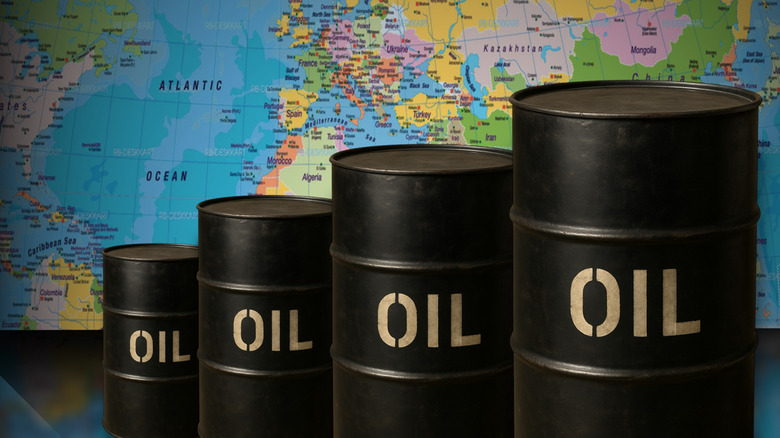 Black barrels filled with oil in front of a world map.