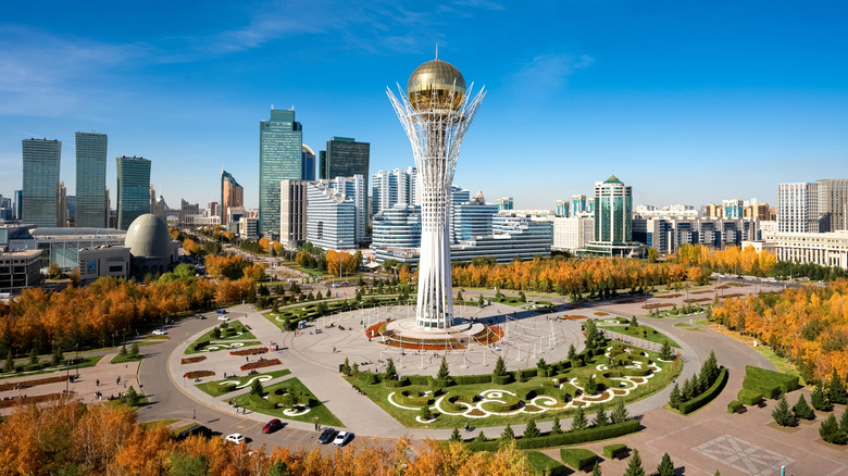Baiterek Tower in Astana, Kazakhstan, rises over a vibrant cityscape with modern skyscrapers and colorful autumn trees.