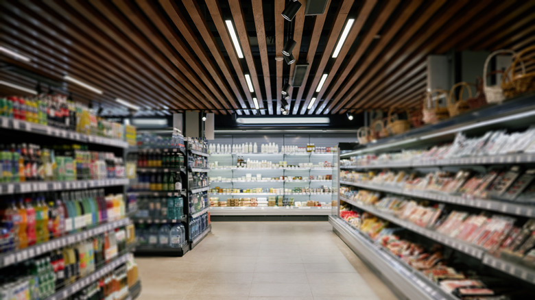 Woman holding bag stands behind cart filled with groceries in 1970s grocery store