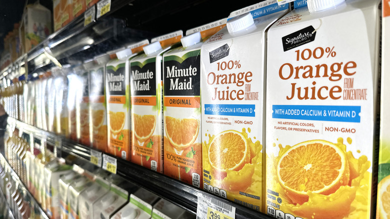 Shelves of name brand orange juice in refrigerated aisle of store