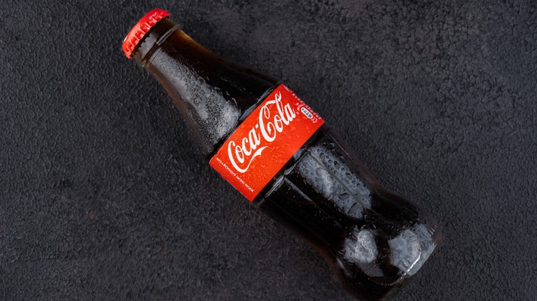 Glass bottle of Coca-Cola, label side up, laying on the ground