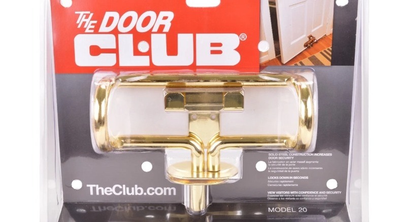 A new brass Door Club home security lock still in its packaging that shows how it works.