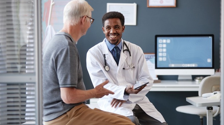 A doctor smiling at an elderly patient with white hair in an office.