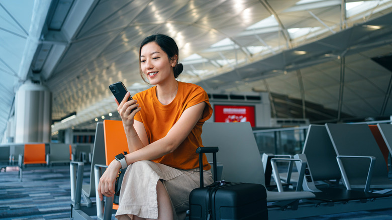 A woman with suitcase using smartphone while waiting for her flight at airport terminal.