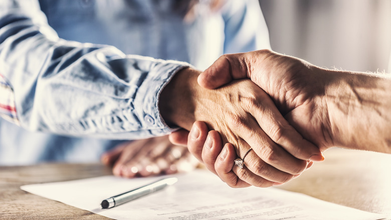 Two people shaking hands over paperwork