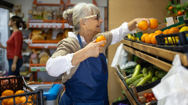 Senior woman stocking grocery shelves with fruit