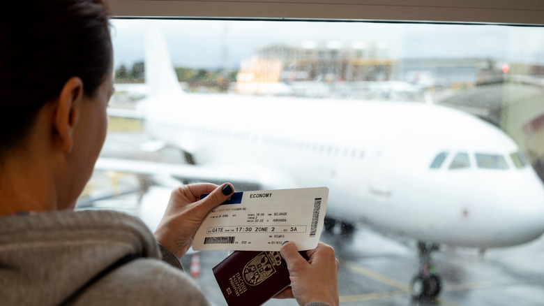 Person holding a ticket in front of an airplane