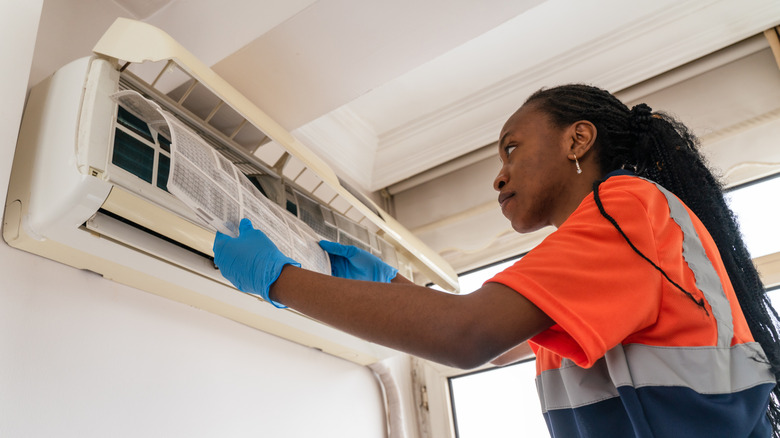 Black woman cleaning air conditioner unit filter