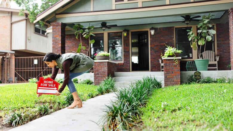 woman putting for sale sign in yard