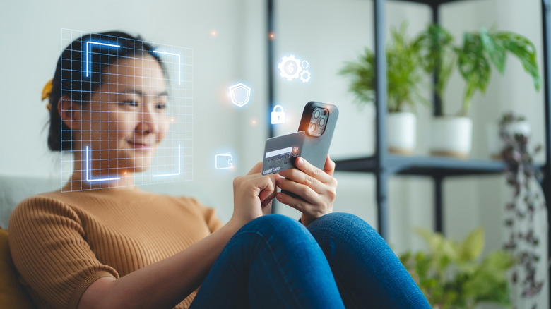 Woman sitting on chair holding credit card while her phone scans her face
