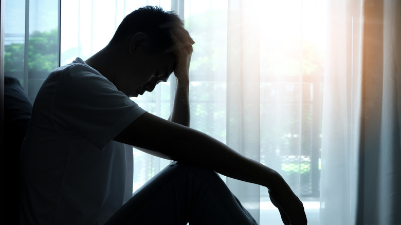 The silhouette of a man sitting on the floor with his head in his hand