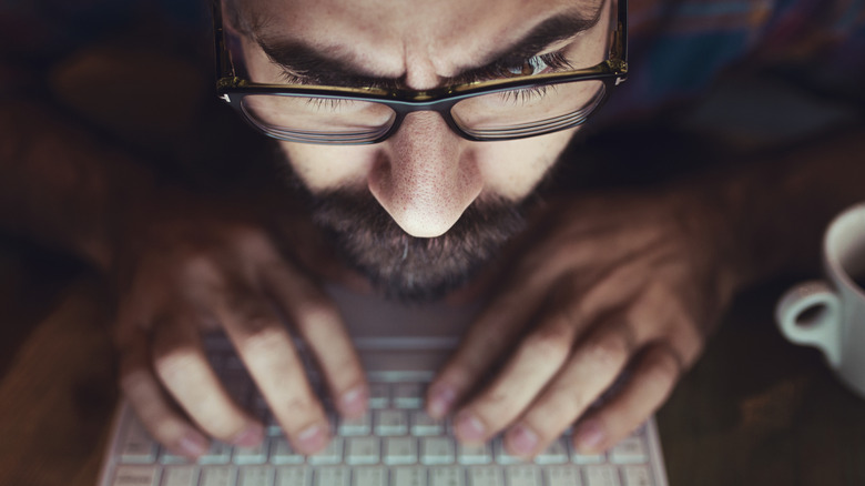close up of man's face leaning close while typing on laptop keyboard