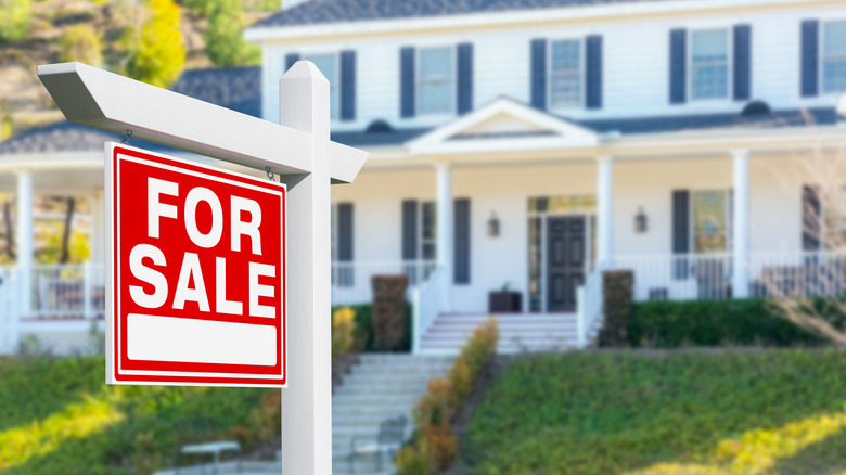A large white house with a "For Sale" sign out front