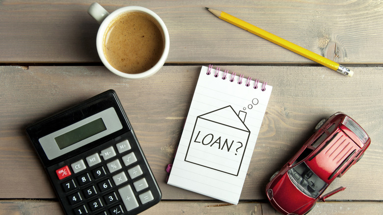 Calculator, cup of coffee, pencil, toy car, and sketchpad with drawing of house around the word "LOAN?"