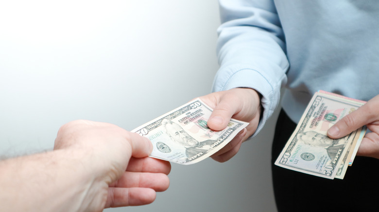 Close up of man holding money in one hand while placing $50 into another man's hand