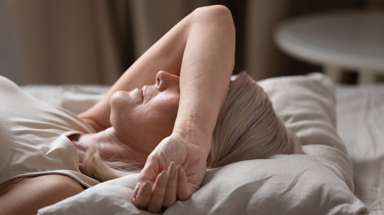A sleeping woman tries to cover her eyes with her bent arm in a bright room