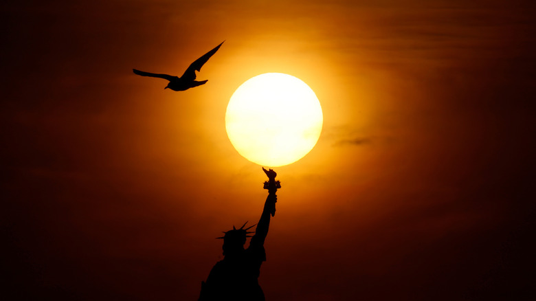 A view of the Statue of Liberty with the sun blazing overhead at sunrise