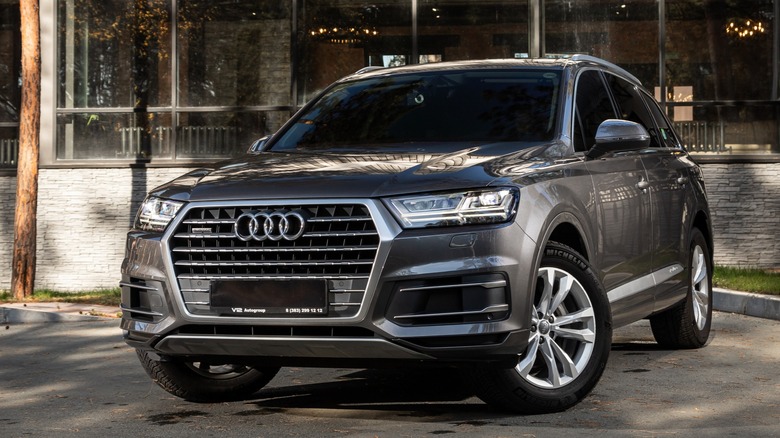 A gray Audi Q7 SUV parked in front of a modern glass building