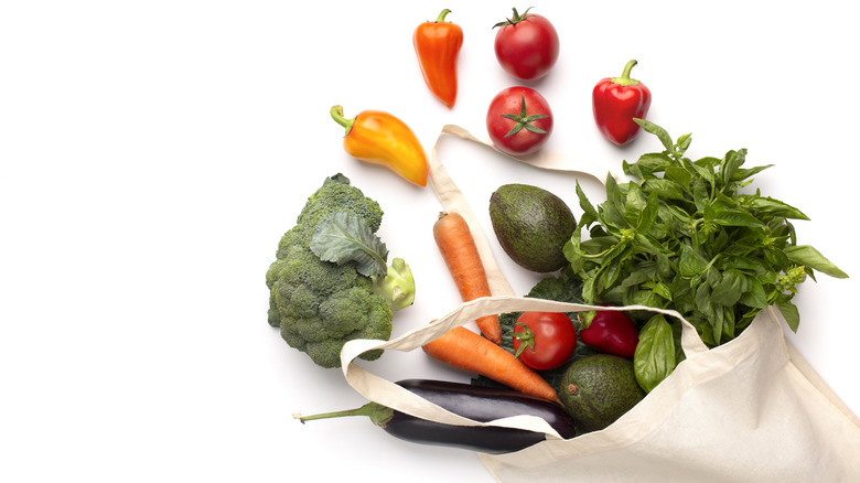 Canvas-colored grocery bag with vegetables spilled across a white background