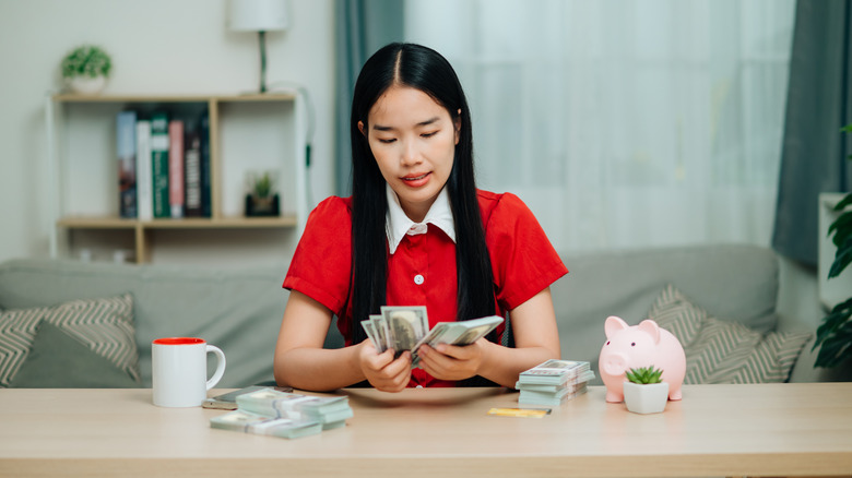 A young woman counting cash next to a piggy bank and a mug